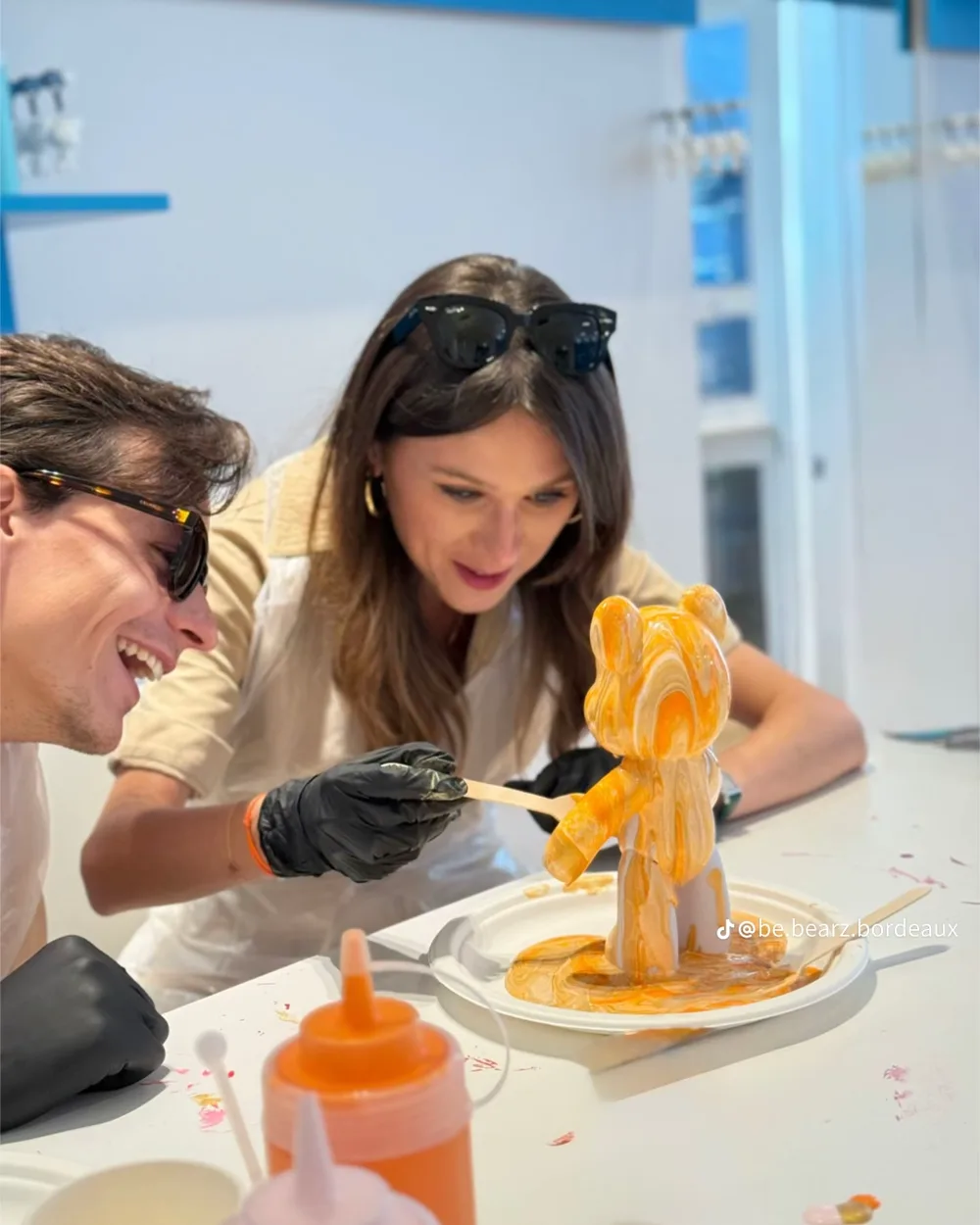 Un couple rit devant un ourson orange en cours de coulée